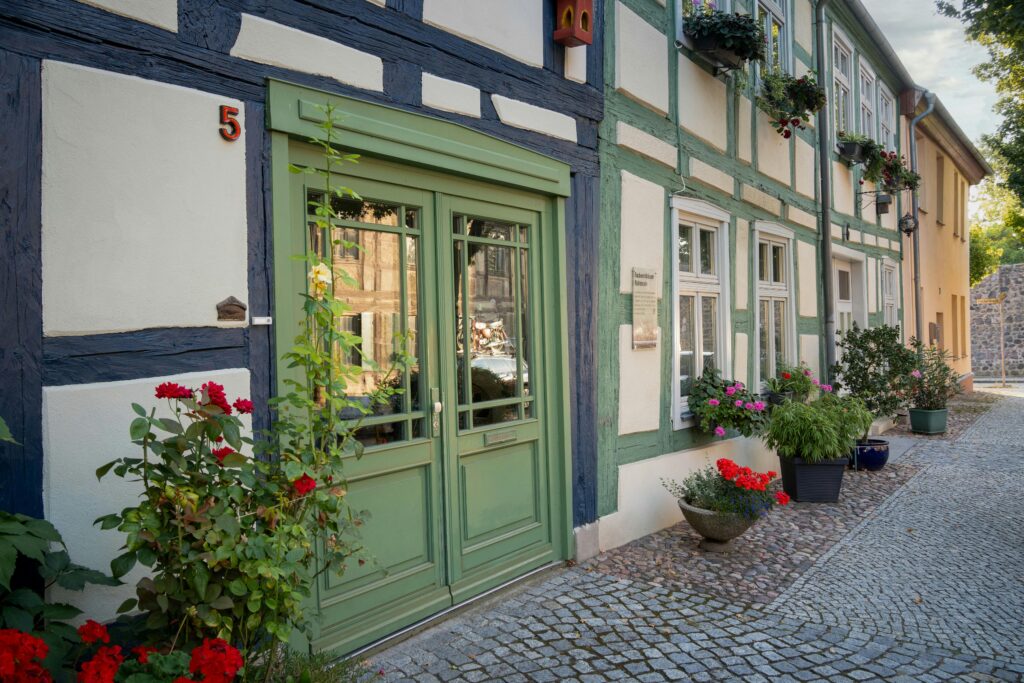 Historic timbered house facade adorned with vibrant flowers on a cobblestone street, showcasing European architecture.